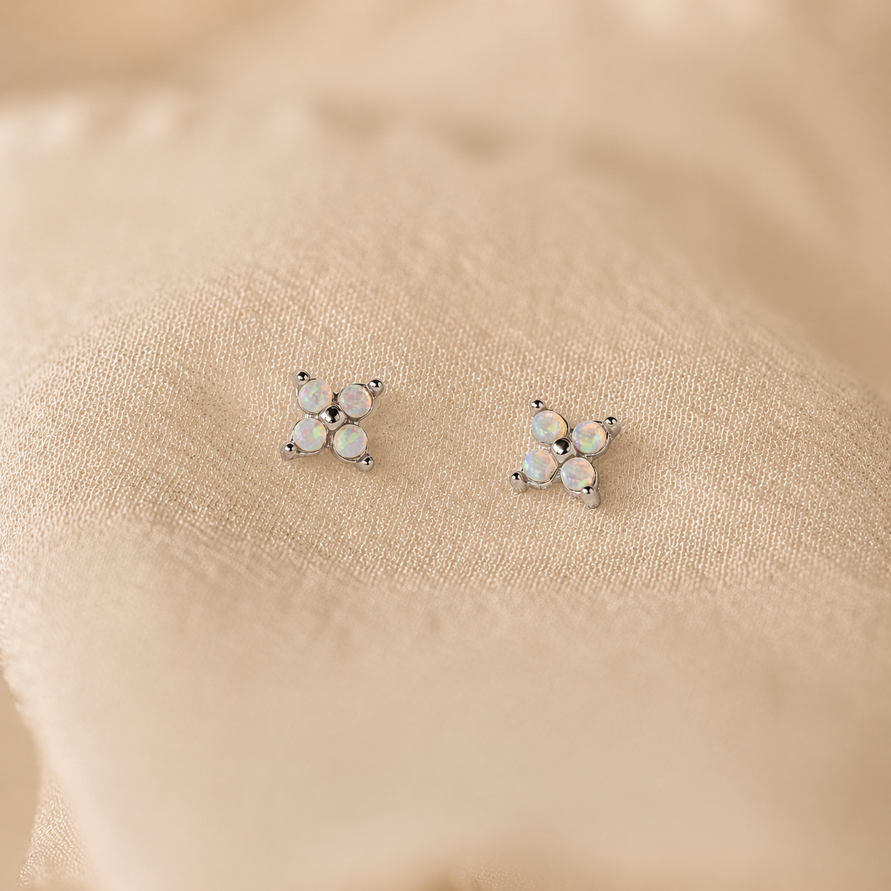 Pair of star-shaped earrings with opal stones on a beige fabric background